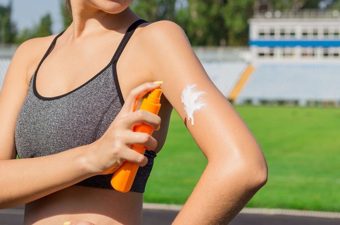 Frau cremt sich vor dem Sport mit Sonnencreme ein.