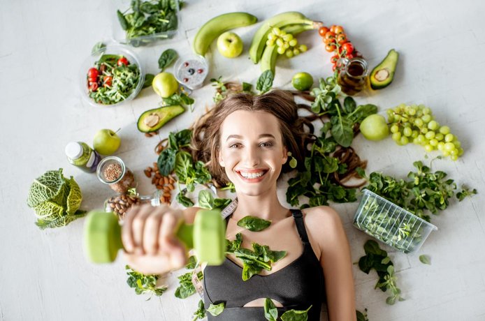 Symbolfoto Frau trainiert mit Hantel, rundherum Salat und Gemüse